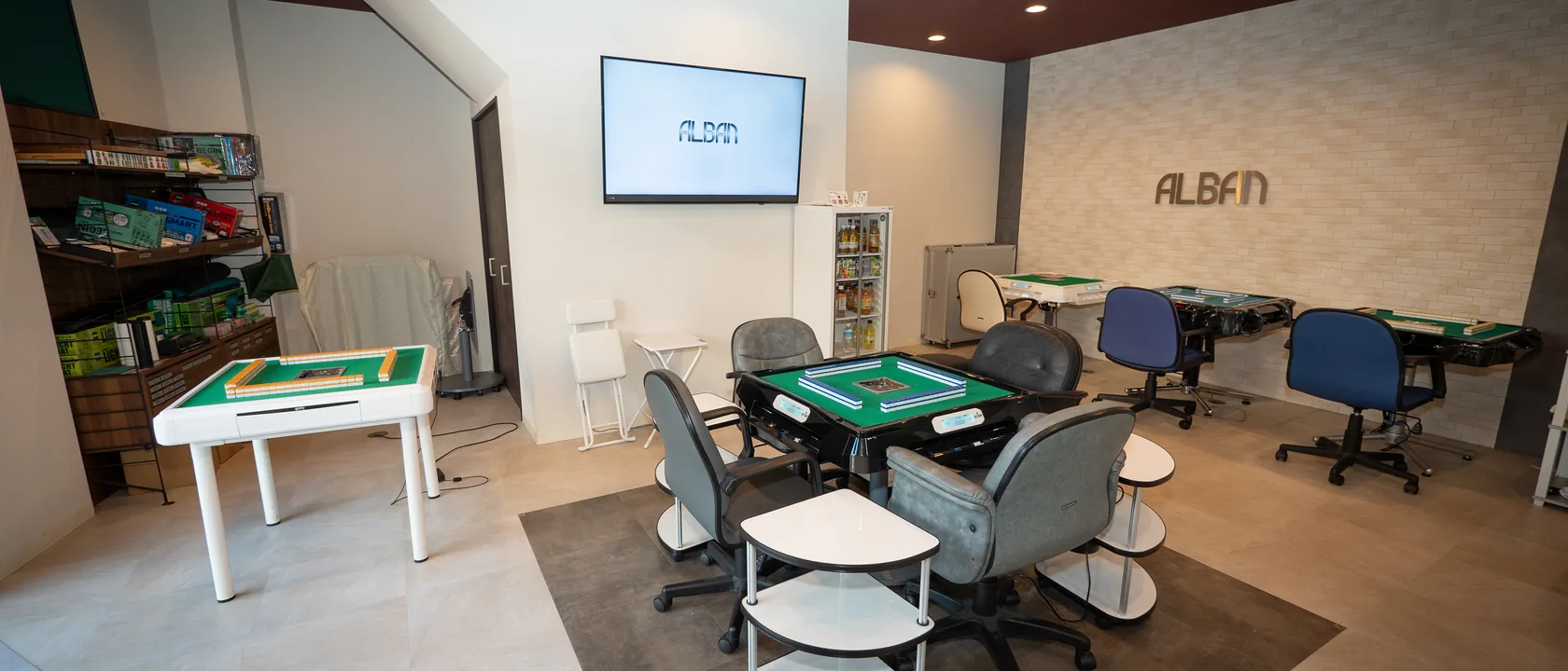 The ALBAN showroom floor in Tokyo: several automatic Riichi tables set up with chairs, the ALBAN name on the brick wall