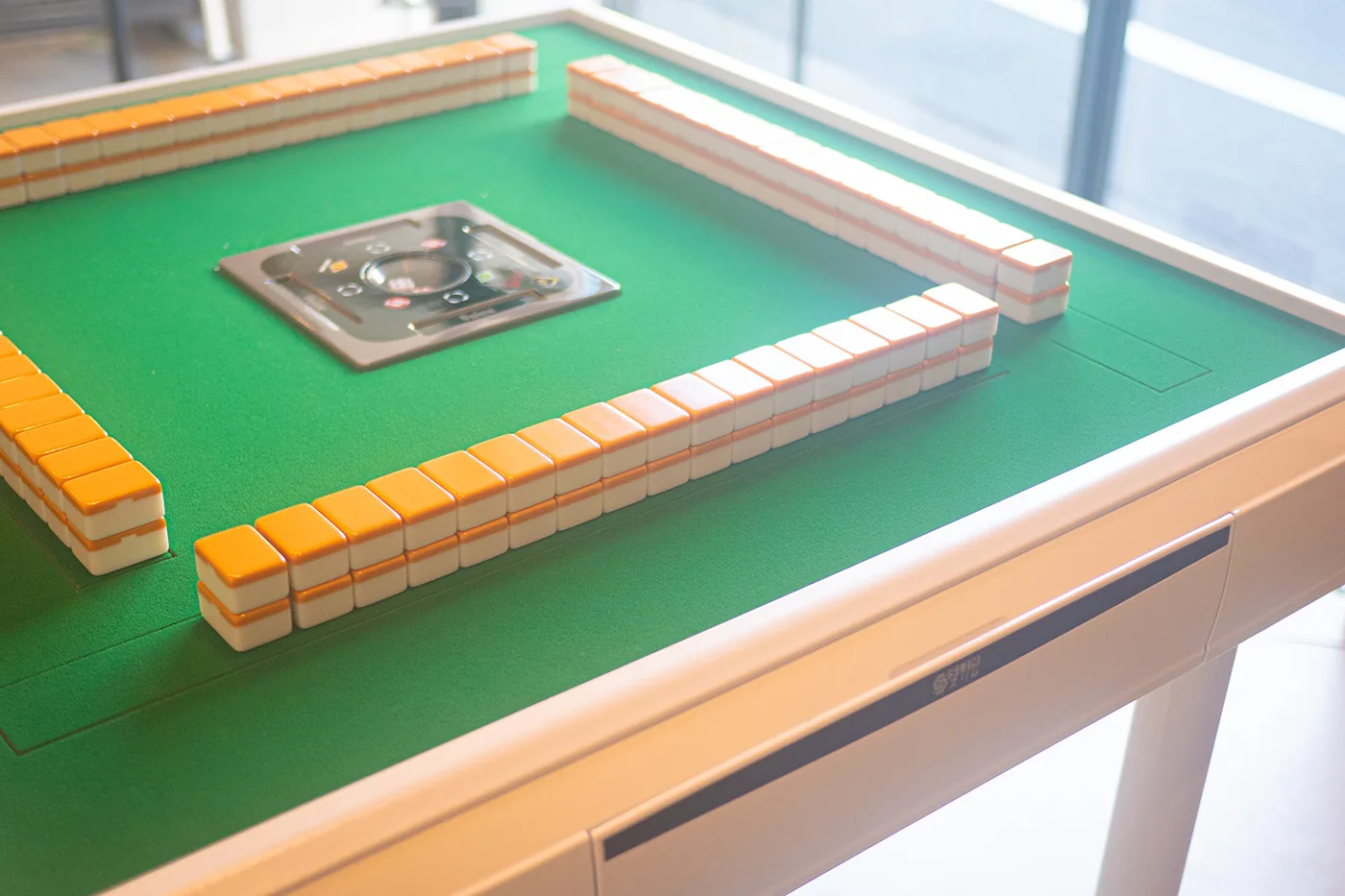 Close-up of mahjong tiles built into a wall on the green felt of an ALBAN table, showing the tile faces, the felt and the table edge